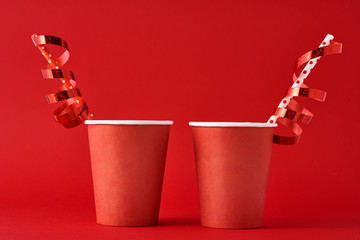 Two paper coffee cups with decorations and straw on the red backgrond. Valentines day festive concept