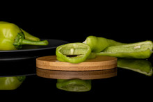 Group Of Two Whole Two Halves Two Slices Of Hot Green Pepper Banana On Round Bamboo Coaster On Gray Ceramic Plate Isolated On Black Glass
