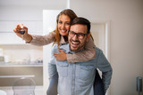 Fototapeta  - Couple showing keys to new home. Young couple holding up new house key. Portrait of young couple feeling happy about buying a new house. Happy couple moving in new home