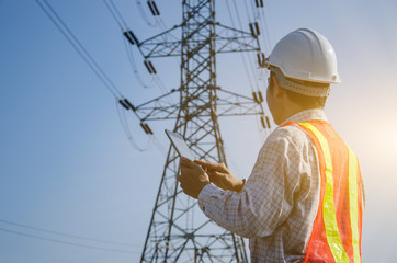 electrical engineer holding and using a digital tablet with high voltage tower background.