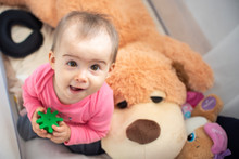 Adorable Baby In Crib Looking Up With Rubber Toy In Hands. Copy Space On Right
