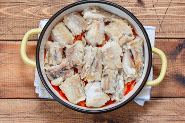 Step by step preparation of pollock in a marinade with onions and carrots, step 4 - preparation for baking fish and vegetables in an enamel form, selective focus, top view