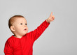 © Dmitry Lobanov - Little toddler boy points finger up side in red infant bodysuit with free text space on gray