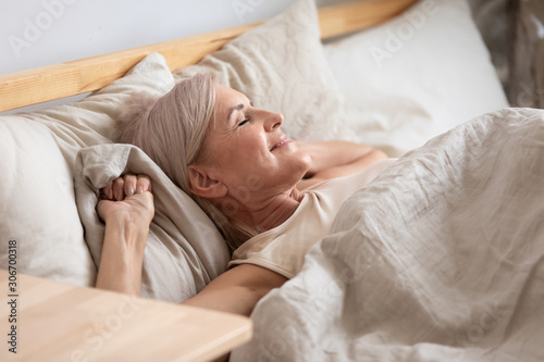 Cuadros en Lienzo Satisfied middle-aged woman lying in bed enjoy early morning