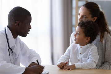 Wall Mural - Young african american male pediatrician listening to little patient complaints.