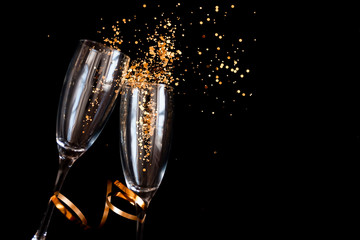 Two champagne glasses with golden sparkles over black background. Happy new year.