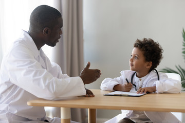 Wall Mural - Happy little patient in doctors uniform plating with pediatrician.