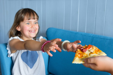 Wall Mural - Hands of a small child and a slice of pizza closeup. The child is out of focus.