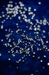 Abstract bokeh pattern of sparkling glass droplets on a dark blue background