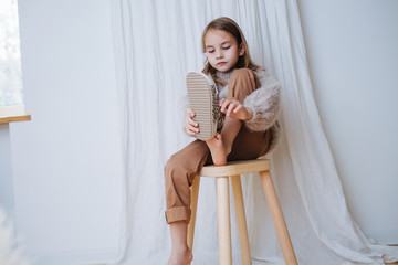 Calm little girl sitting on a stool at home, she's puting on sandals