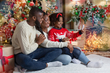 Wall Mural - Little black girl taking selfie with parents near Christmas tree