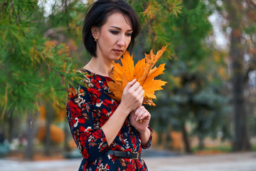 Wall Mural - Beautiful elegant woman standing and posing with bouquet of yellow leaves in autumn city park