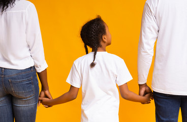 Wall Mural - Rear view of african mother, father and daughter holding hands together