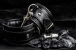 Leather handcuffs, anal plug, latex gloves on black background.