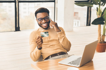 Black man holding credit card and talking on cellphone