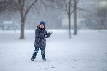 A little boy in a hat and jacket laughs and rejoices in the winter snow .