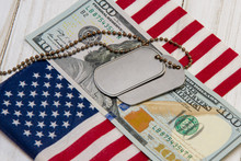 Against The Background Of The American Flag And Dollar Bills Lie Army Identification Medallions. Concept: Military Pension, Salary In The Army, Insurance For The Military, Mercenaries And Contractors.