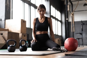 Young woman sitting on floor after her workout and looking down. Female athlete taking rest after fitness training