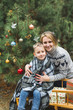 © sofiko14 - Mother with little son in winter park sledging. Mom and child sitting together on wooden decorated sledge with Christmas presents. Winter walk outdoors, decorated Christmas tree
