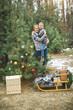 © sofiko14 - Pretty young mother holding her son standing near the decorated Christmas tree in winter forest outdoors. Wooden sledge and present boxes under the tree