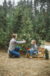 © sofiko14 - Winter and people concept - mother with child son decorates a christmas tree outdoors in the forest. The boy is sitting on the wodden sledge and drinking hot drink