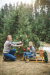 © sofiko14 - Winter and people concept - mother with child son decorates a christmas tree outdoors in the forest. The boy is sitting on the wodden sledge and drinking hot drink