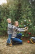 © sofiko14 - Mother and little son looking at camera and smiling, while decorate Christmas tree in winter forest, outdoors. New Year decorations, wooden sledge, present gifts