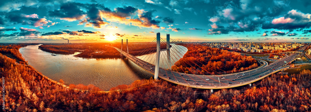 Beautiful panoramic aerial drone view to cable-stayed Siekierkowski Bridge over the Vistula river and Warsaw City skyscrapers, Poland in gold red autumn colors in November evening at sunset - obrazy, fototapety, plakaty 
