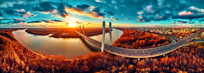 Beautiful panoramic aerial drone view to cable-stayed Siekierkowski Bridge over the Vistula river and Warsaw City skyscrapers, Poland in gold red autumn colors in November evening at sunset