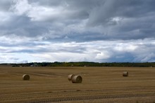 Dark Clouds Of A Storm Front Loom Over A Field With Round Bales