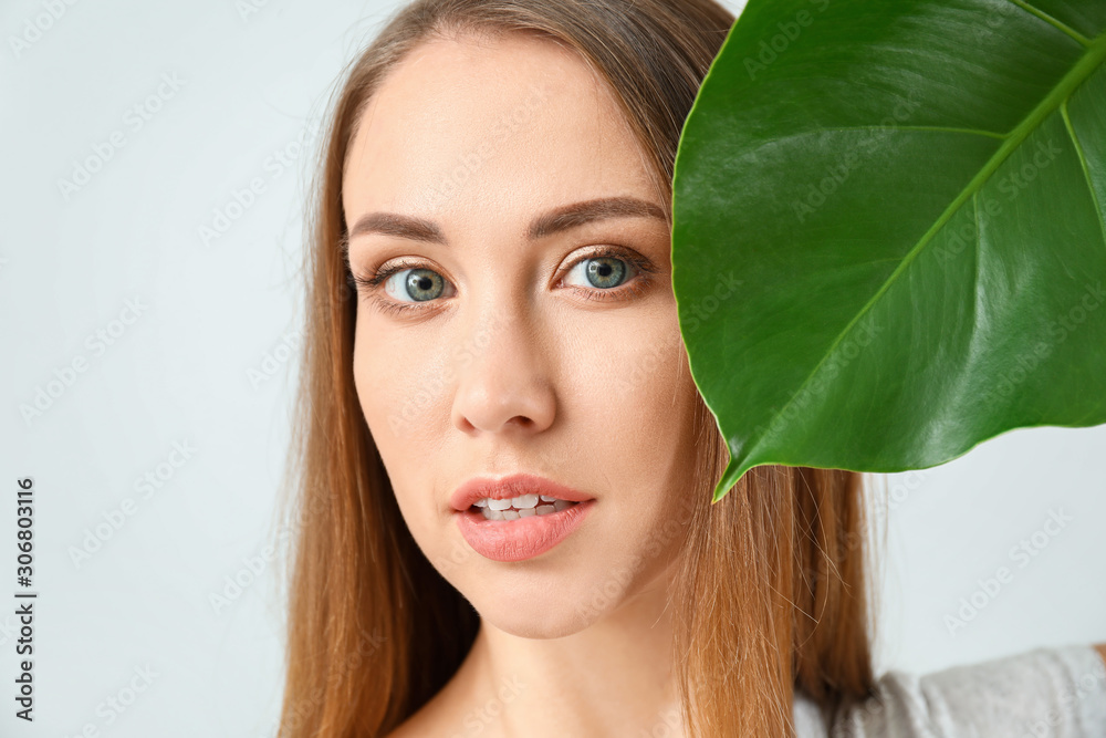 Beautiful young woman with tropical leaf on light background