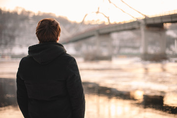 back view of thoughtful young man standing by river in winter