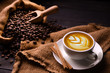 Cup of coffee latte and coffee beans in burlap sack on old wooden background