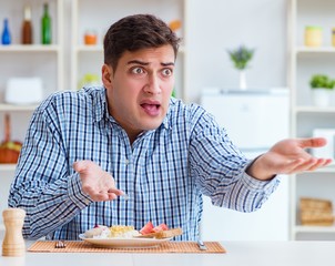 Wall Mural - Young husband eating tasteless food at home for lunch