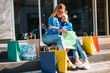 © Serhii - Beautiful mom and her cute little daughter are holding shopping bags, looking at camera and smiling while standing outdoors. Shopping concept.