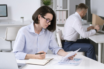 Poster - Busy female office manager looking through papers and making notes by desk