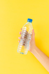 Woman’s hand holding small plastic bottle of water on yellow background