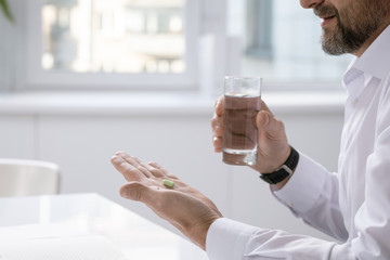 Poster - Hands of businessman holding pill while going to take it and glass of water