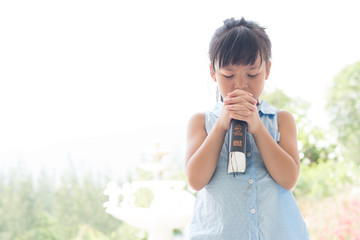 Wall Mural - Cute asian little girl closed her eyes and folded her hand in prayer on a Holy Bible for faith concept