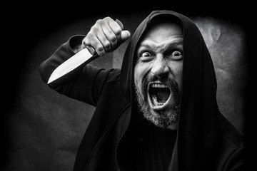 Black and white portrait of a bald bearded man in a hood on a dirty gray background. Maniac with a knife concept.