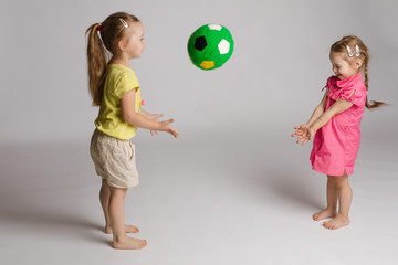 Side view of two cheerful kids throwing and catching ball on isolated background. Beautiful sisters looking at each other, playing and laughing. Concept of happiness and game.