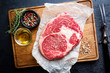 Raw fresh meat Ribeye Steak and seasonings on dark background, top view with copy space