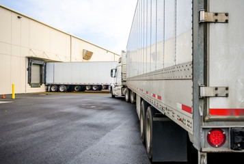 Big rig semi truck with a dry van semi trailer is turning on the warehouse parking lot to park the trailer to the gate in the loading dock