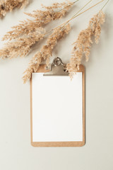 Wall Mural - Flat lay minimalist home office desk with blank sheet clipboard with copy space for text, reeds branch, casket on neutral background. Top view work, business, education template.