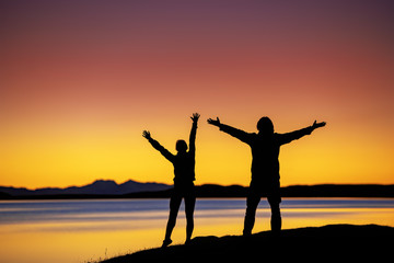 Wall Mural - silhouettes of two hikers with raised arms against sunset