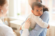 © AnnaStills - Young mother holding her little child on her hands while female doctor examining him with stethoscope at hospital