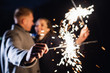 Selective focus of sparklers in hands of young couple enjoying holiday time outdoors