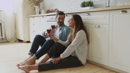 Wall Mural - Happy couple hold glasses drink wine sit on kitchen floor