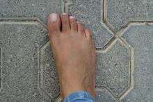 Close Up Of Women's Foot Isolated On A Concrete Floor Background. Foot Is Ugly, Dark Brown And It Has Hair And Veins Showing. No Manicure. Unmanicured Nails.