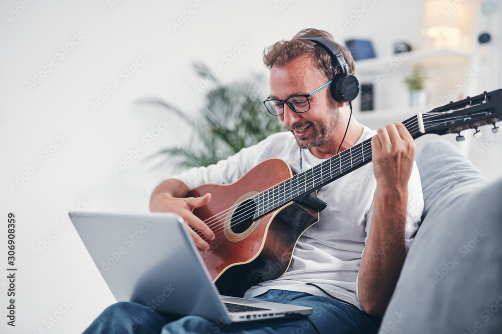 Man playing acoustic guitar in the living room. - obrazy, fototapety, plakaty 